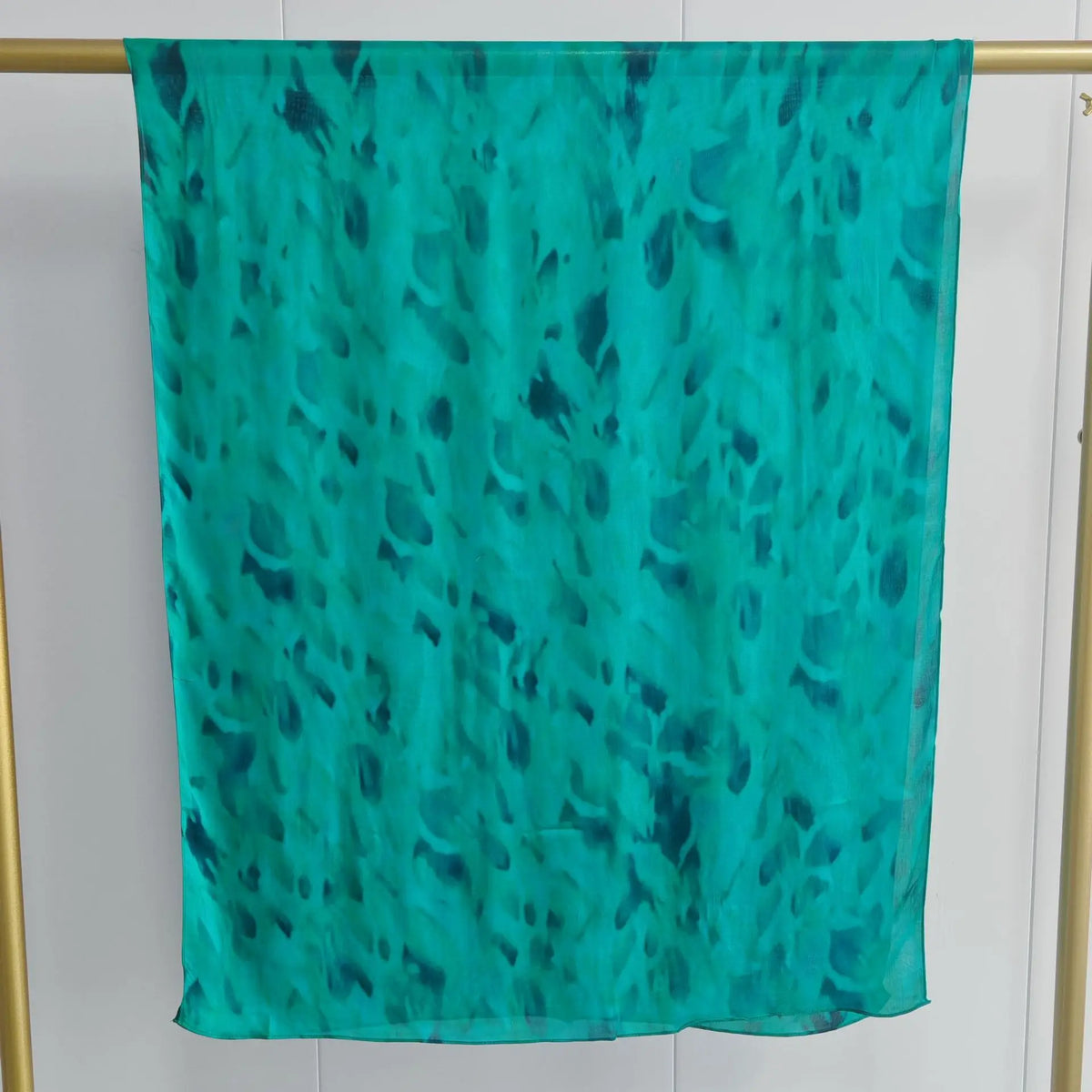 Türkis durchscheinender Schal mit blauem Aquarellmuster vor hellem Hintergrund.