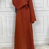 Eine Frau in einem eleganten, langärmeligen, rostfarbenen Maxi-Abaya-Kleid.