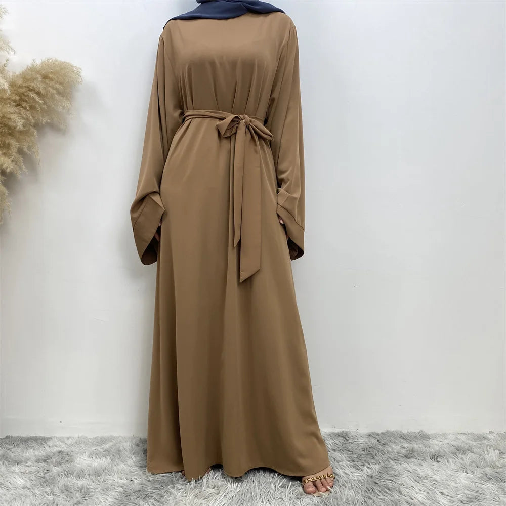 Una abaya beige fluida para mujeres con cintura atada y un pañuelo azul para la cabeza.