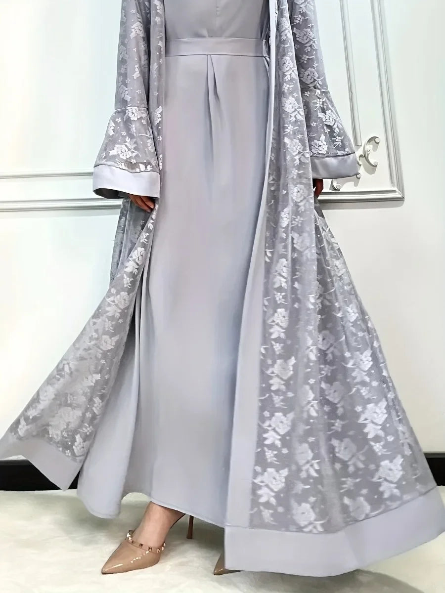 Une femme portant un ensemble abaya en dentelle gris clair avec une jupe et une tunique assorties.