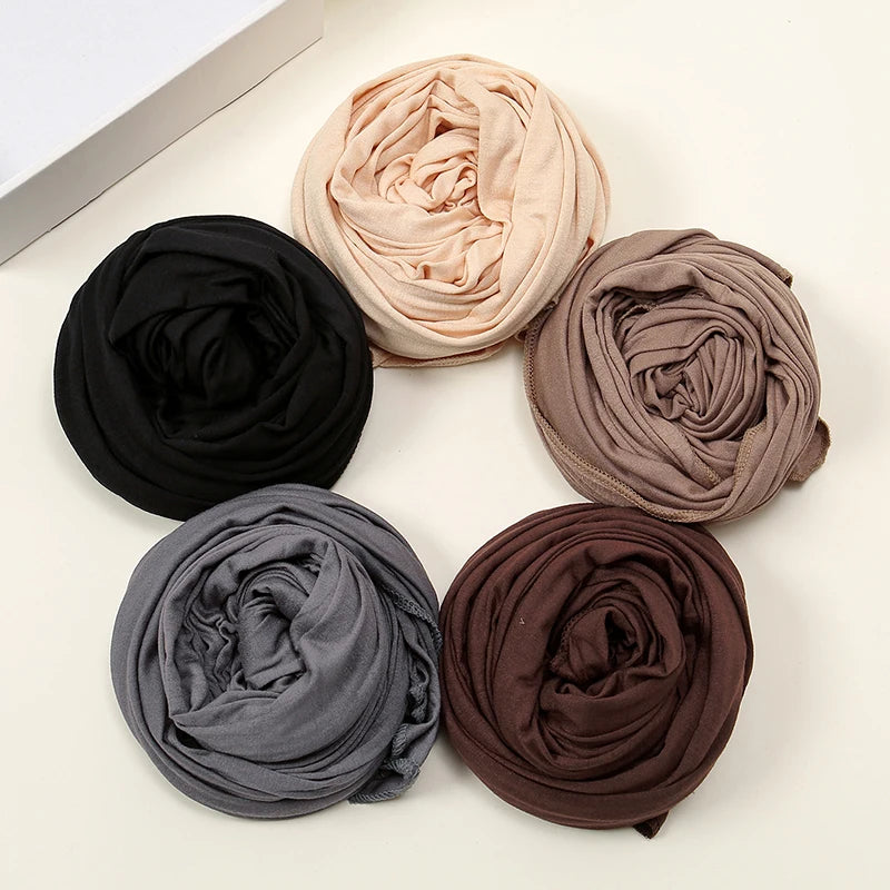 Collection de cinq foulards de hijab en tissu solide roulés dans les tons de noir, beige, taupe, gris et marron.