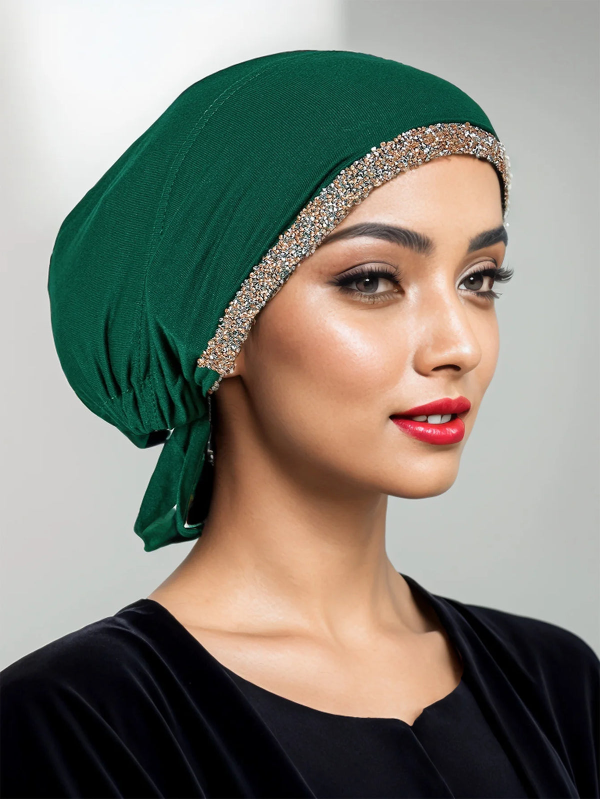 Eine Frau trägt eine elegante smaragdgrüne Hijab-Kappe mit einem funkelnden Strassband und einem schwarzen Kleidungsstück.