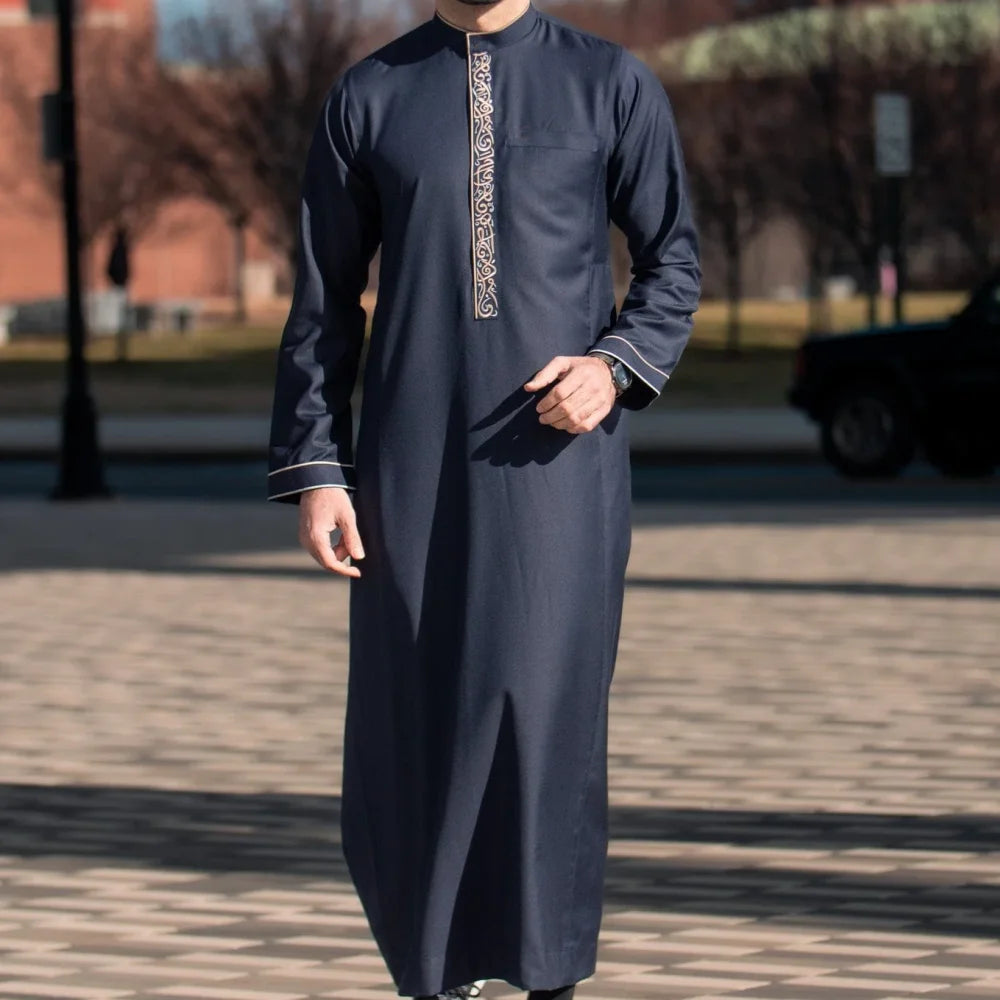 Un homme portant une robe musulmane bleu foncé avec broderie rétro verticale, debout à l'extérieur.