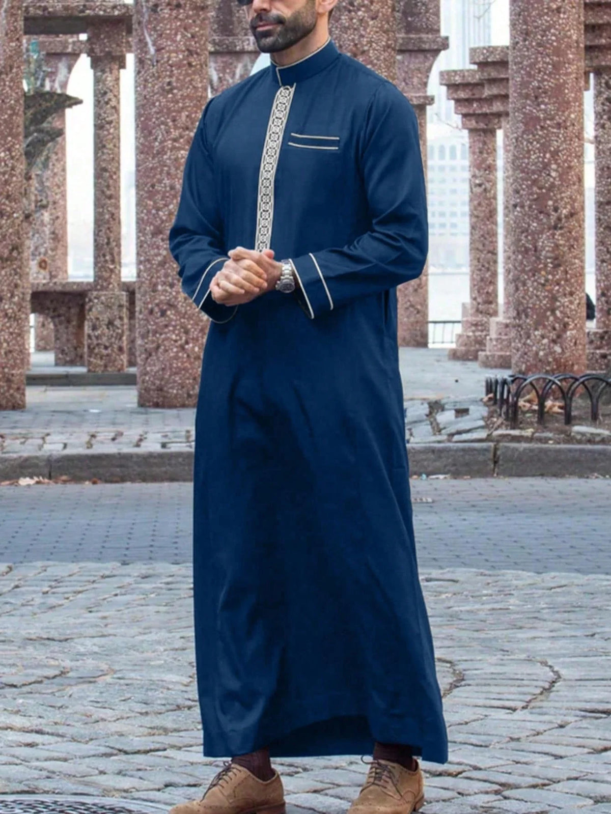 Mann in dunkelblauem besticktem Langarm-Arabischer Thobe im Freien stehend.