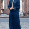 A man wearing a dark blue Moroccan ethnic thobe with a stand collar and gold embroidery, standing outdoors.