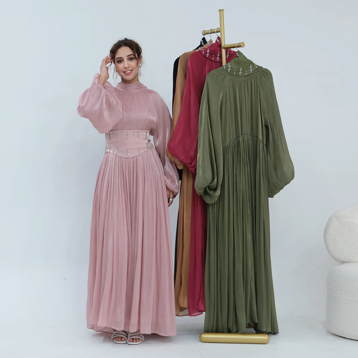 Une femme modélise une abaya rose poudré fluide avec un ceinturon orné, à côté d'une abaya verte.