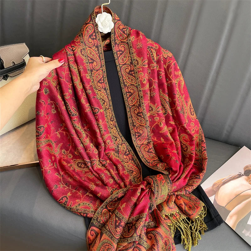 Una pashmina de lujo con patrón rojo y dorado vibrante drapeada alrededor del cuello de una persona.