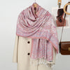 Chal de bordado paisley rosa y blanco sobre un abrigo beige, con un bolso de cuero marrón cercano.