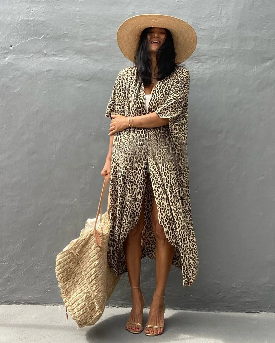 Eine Frau in einem langärmeligen Leopardenmuster-Kimono-Überkleid und einem breiten Strohhut vor einer grauen Wand.