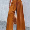 Un mannequin porte un pantalon large couleur rouille avec un élastique à la taille et des détails en dentelle, associé à un h