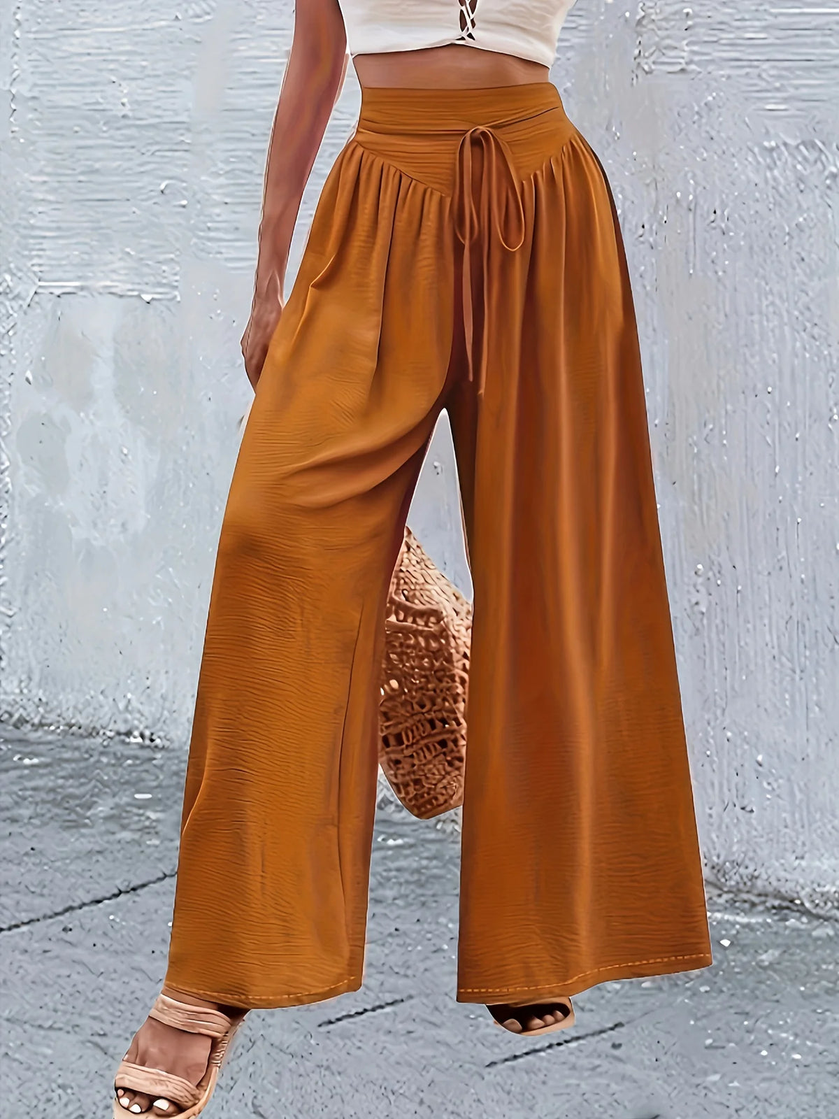 Un mannequin porte un pantalon large couleur rouille avec un élastique à la taille et des détails en dentelle, associé à un h