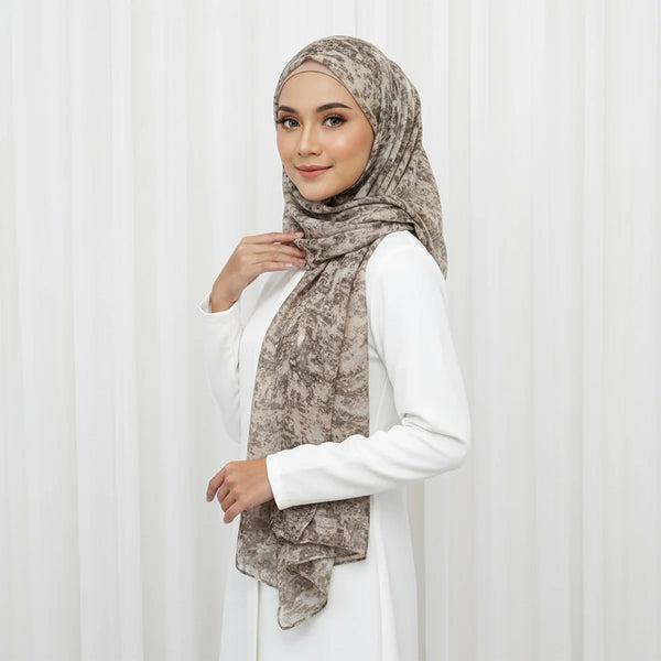 A woman wearing an elegant floral viscose hijab scarf in beige tones and a white outfit.