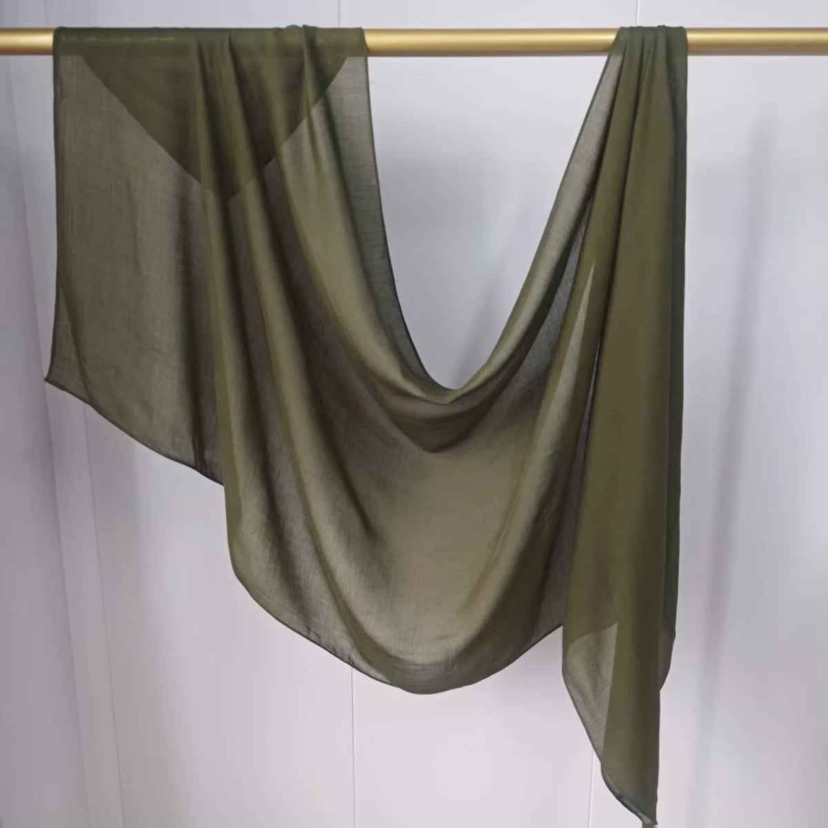 Foulard hijab modal vert olive transparent drapé sur un cintre doré.