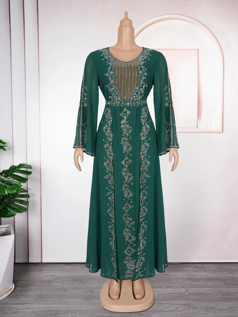 A full-length emerald green maxi dress with gold embroidery and sequins displayed on a mannequin.