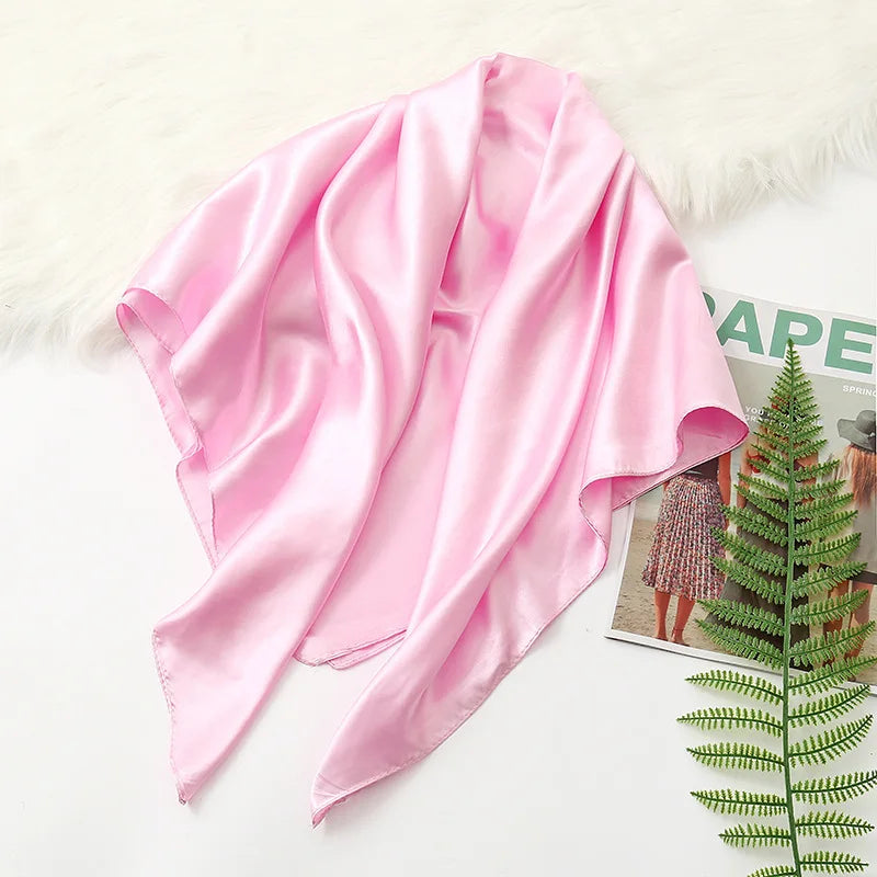 A flowing pink silk satin hijab scarf draped over a white fluffy surface.