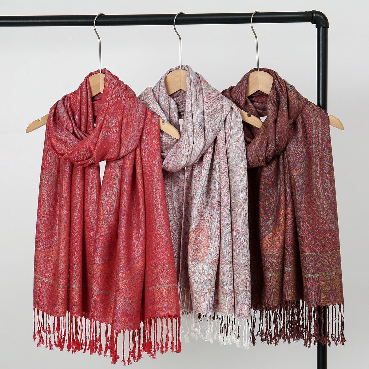 Exhibición de tres pañuelos/chalinas vintage de bordado paisley en tonos rojos, rosa y marrón colgados en un perchero.
