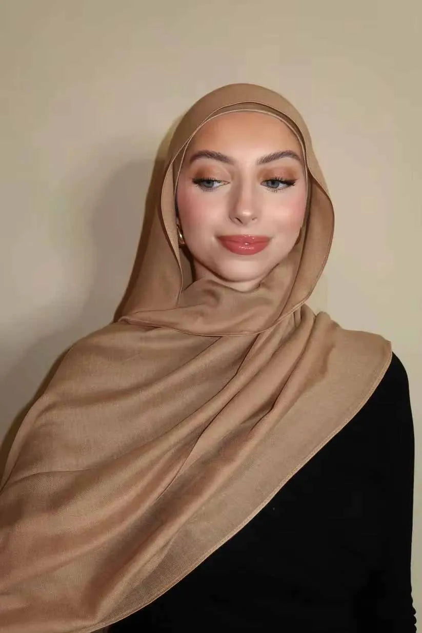 Eine Frau trägt einen beige-gradienten Rayon-Modal-Hijabschal und schwarze Kleidung.