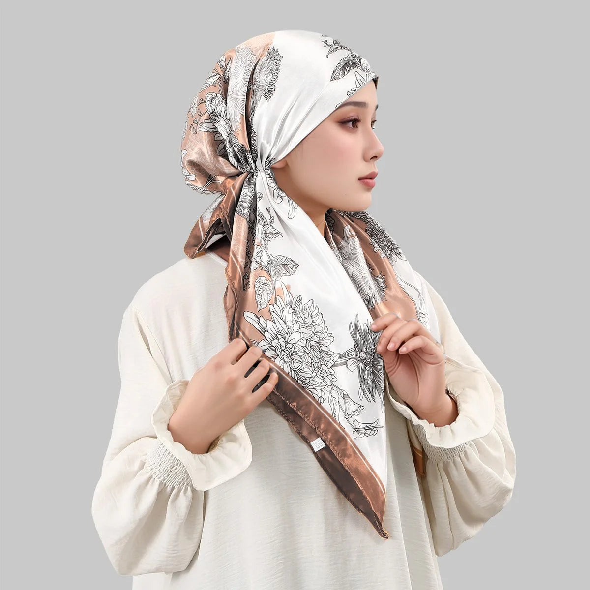 A woman wearing an elegant satin silk instant hijab scarf with a floral print in beige and brown tones.