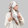 Eine Frau trägt einen satinigen Seiden-Instant-Hijab mit floralem Muster in beige- und braunen Tönen.