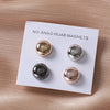 A white card displaying two gold and silver macaron brooches for hijab clips.