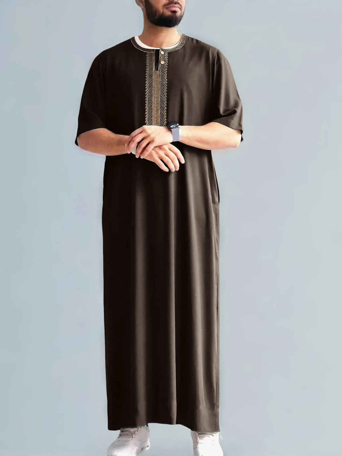 Ein Mann trägt ein dunkelbraunes besticktes Jubbah Thobe mit silbernem Kragen und weißen Hosen.