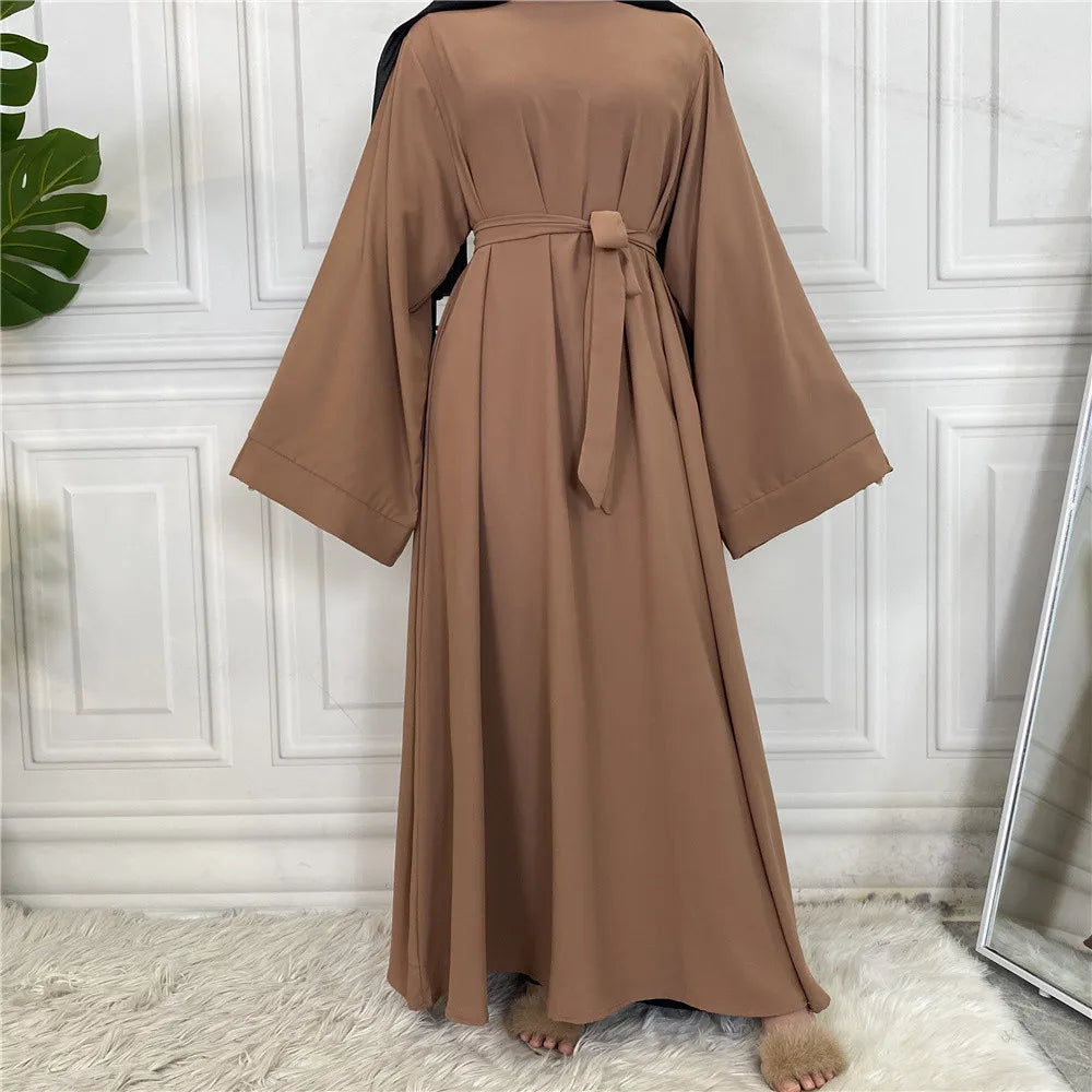 Lange, lockere braune Abaya für Frauen mit gebundener Taille, vor weiß verkleidetem Wand
