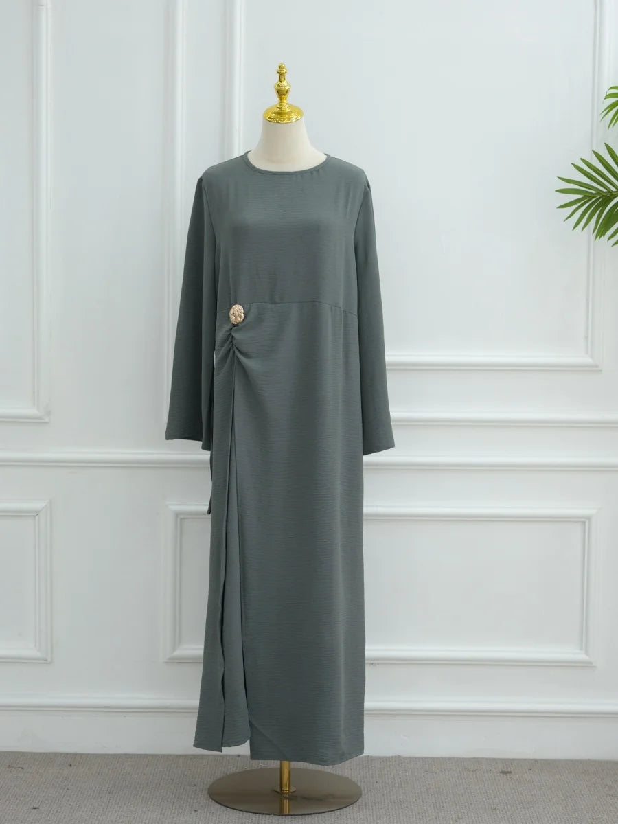 Une longue abaya gris uni présentée sur un mannequin devant un mur blanc.
