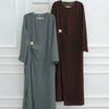 Une abaya longue à manches longues brun foncé pour femmes, présentée sur un cintre contre un mur blanc.