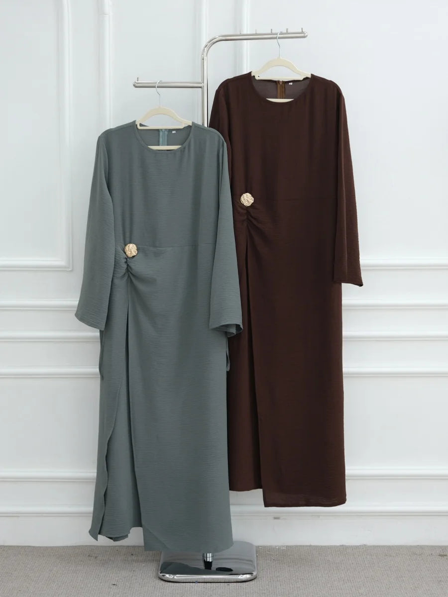 Une abaya longue à manches longues brun foncé pour femmes, présentée sur un cintre contre un mur blanc.