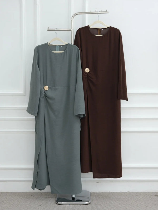 A dark brown, long-sleeved abaya for women displayed on a hanger against a white wall.