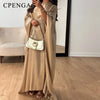 Eine Frau in einem eleganten, fließenden beige langen Oberteil und einer weißen Lederhandtasche.