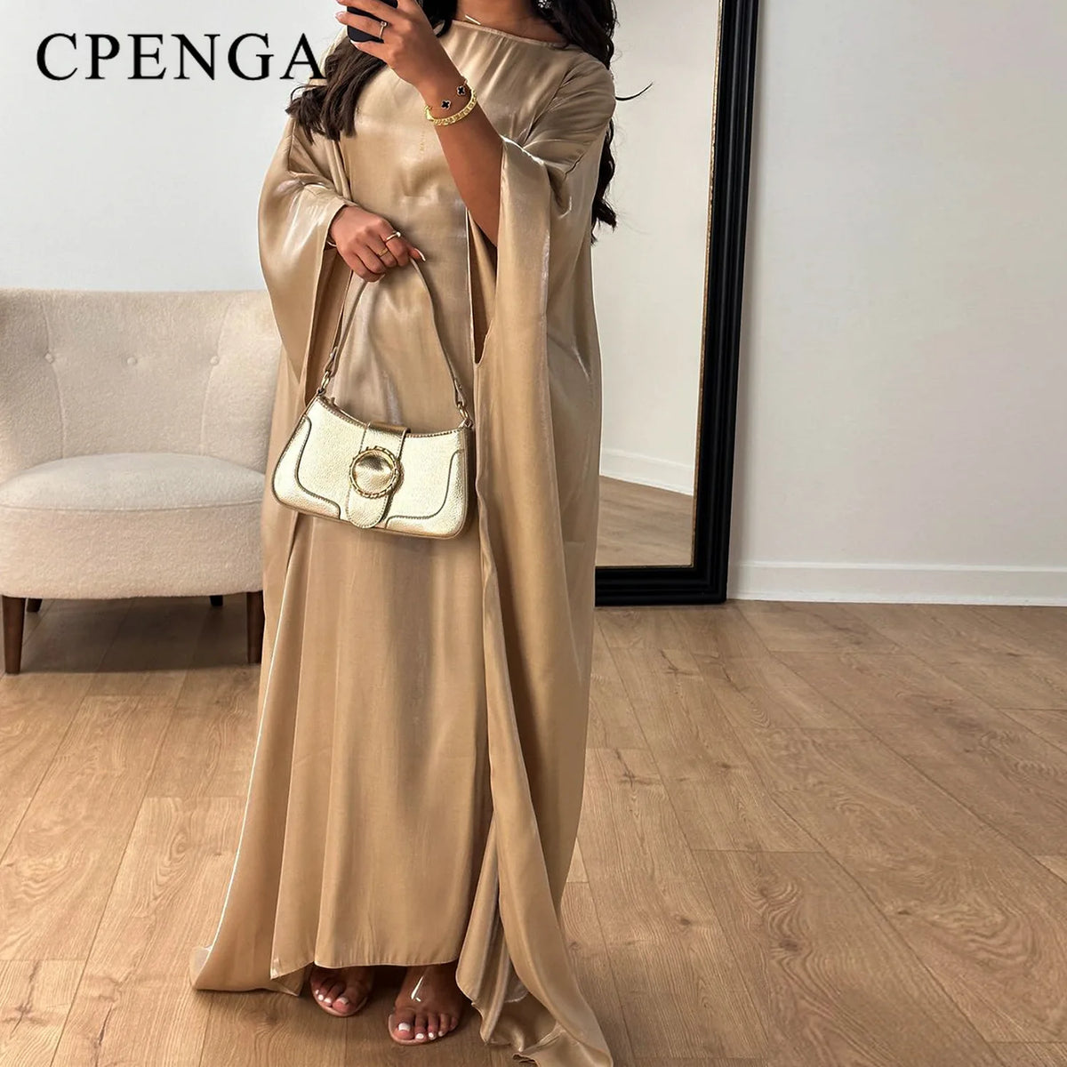 Eine Frau in einem eleganten, fließenden beige langen Oberteil und einer weißen Lederhandtasche.
