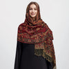 Una mujer vistiendo un pañuelo pashmina de lujo con estampado rojo intenso y dorado sobre una prenda negra.
