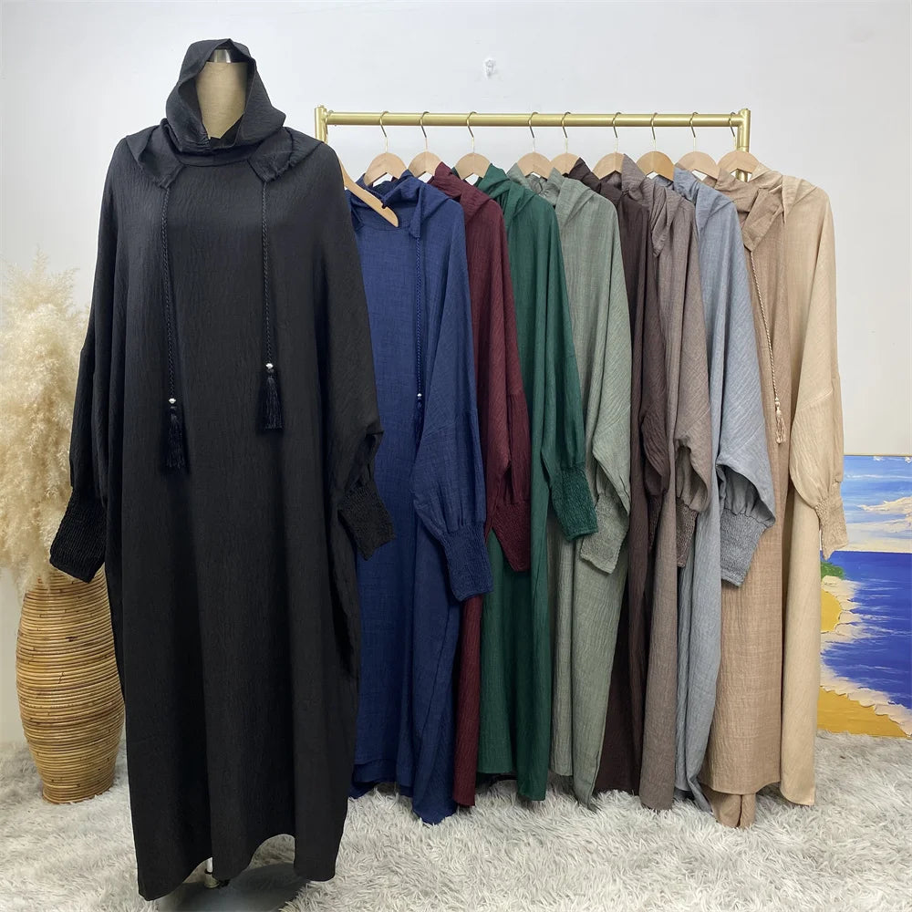Abaya multicolore avec capuche et manches batwing, exposée sur cintre en bois sur fond blanc.