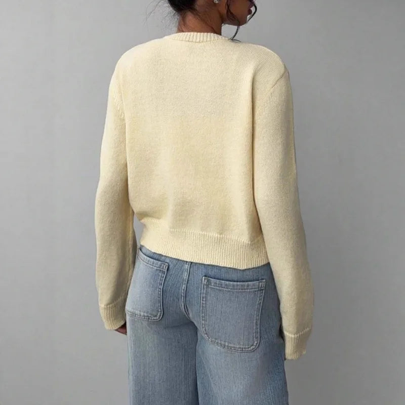 Une femme portant un pull tricoté de couleur crème et un jean bleu, vue de dos.