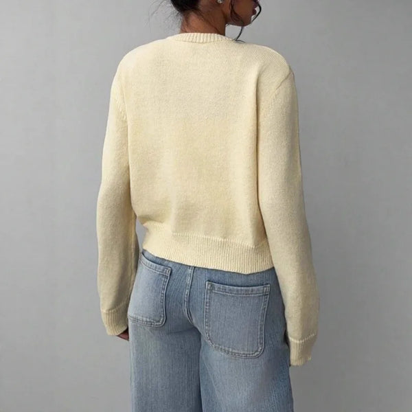 A woman wearing a cream-colored knit sweater and blue jeans, shown from the back.