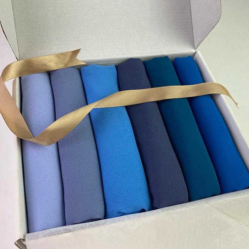 Eine Box mit einer Sechspackung blauer und lila Chiffon-Hijabs mit goldenen Bandverschlüssen.