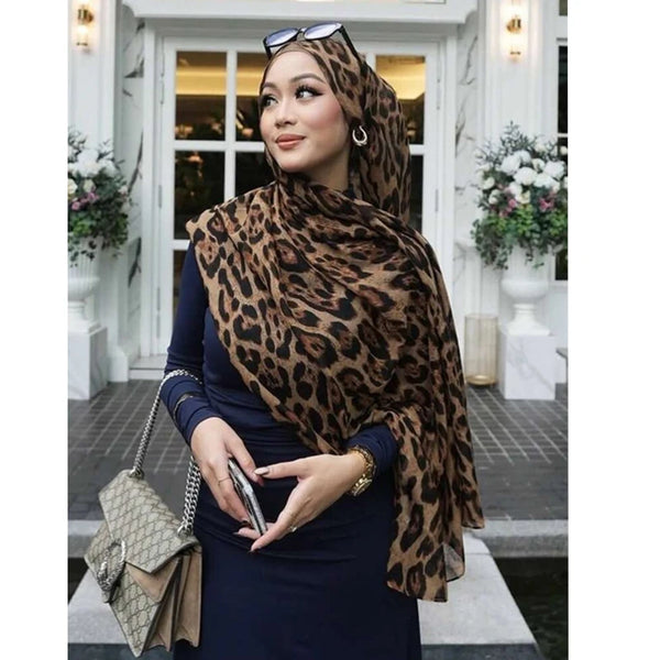 A woman wearing a leopard print pashmina shawl and dark blue dress posing in front of a white door.
