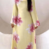 A woman wearing a long, yellow kaftan dress with a floral print featuring pink and white flowers.