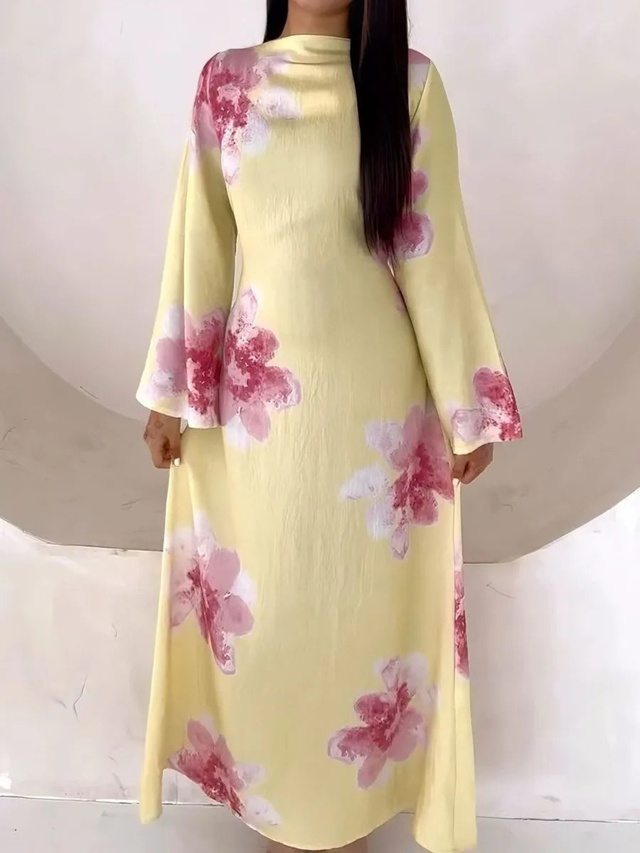 A woman wearing a long, yellow kaftan dress with a floral print featuring pink and white flowers.