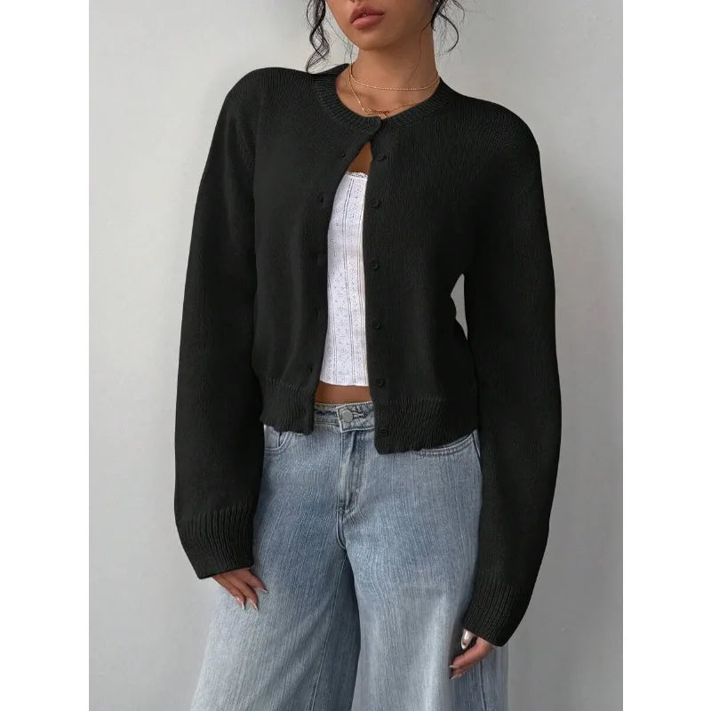 Une femme portant un pull en tricot noir par-dessus un haut blanc et un jean délavé clair.