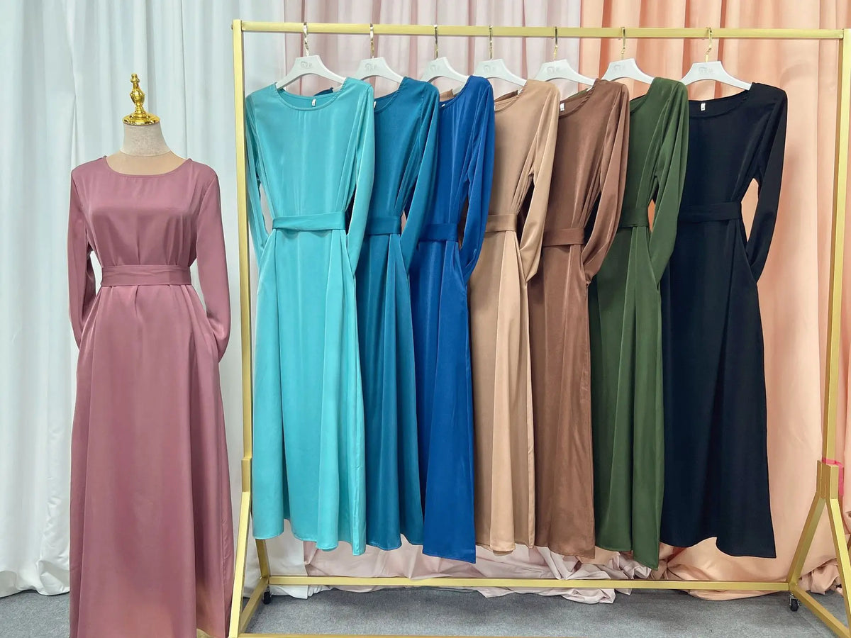 Eine Präsentation fließender, bodenlanger Abayas in verschiedenen Blautönen, Beige- und Olivgrüntönen, aufgehängt an einem go