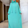 Una mujer vistiendo una abaya de algodón verde menta con lunares negros y una capucha a juego con decoración floral.