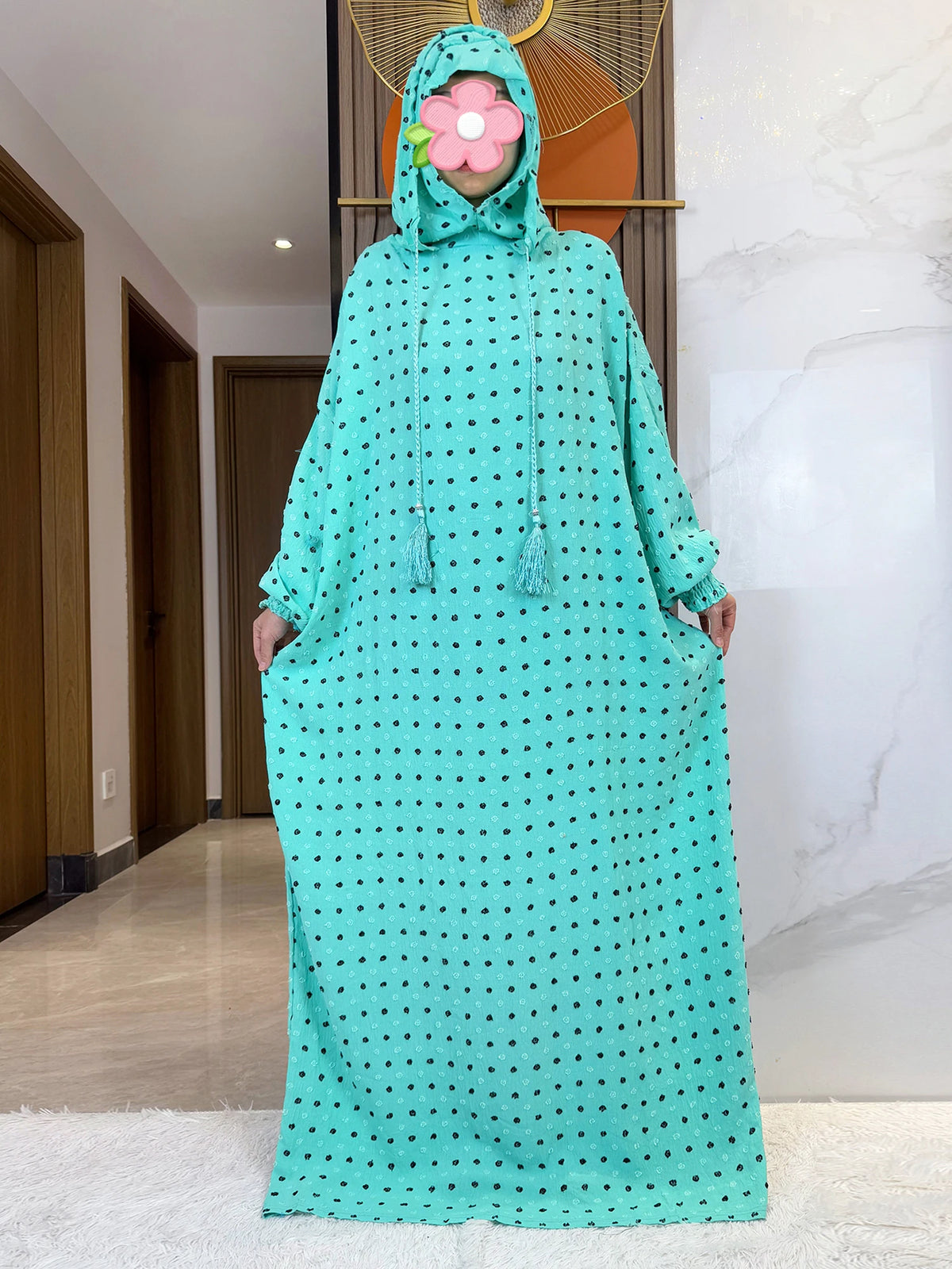 Una mujer vistiendo una abaya de algodón verde menta con lunares negros y una capucha a juego con decoración floral.