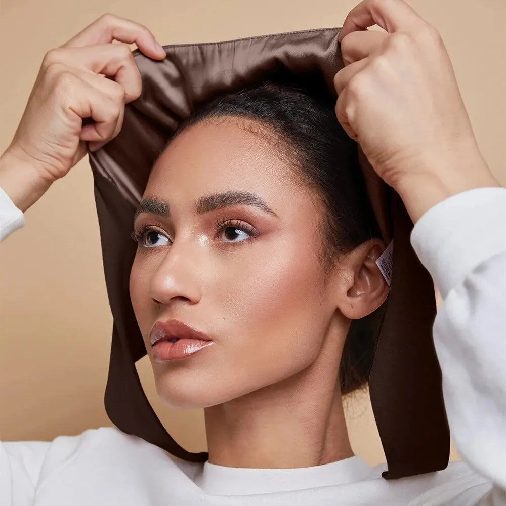 A woman is adjusting an elegant satin hijab cap and undercap set on her head.