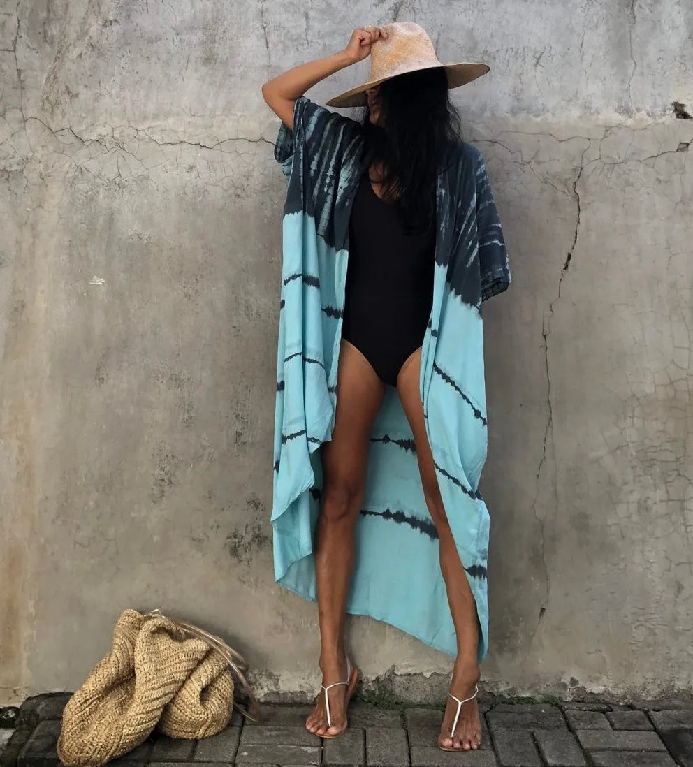 Eine Frau in hellem Beige und einem blau-schwarz gestreiften Kimono-Überwurfkleid vor einer strukturierten Wand.