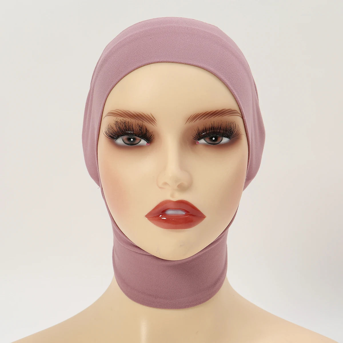 A model wearing a mauve inner hijab cap scarf with long eyelashes and glossy orange-red lips.