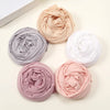 Collection de foulards de hijab unis roulés en beige, gris, blanc et rose, disposés en cercle.