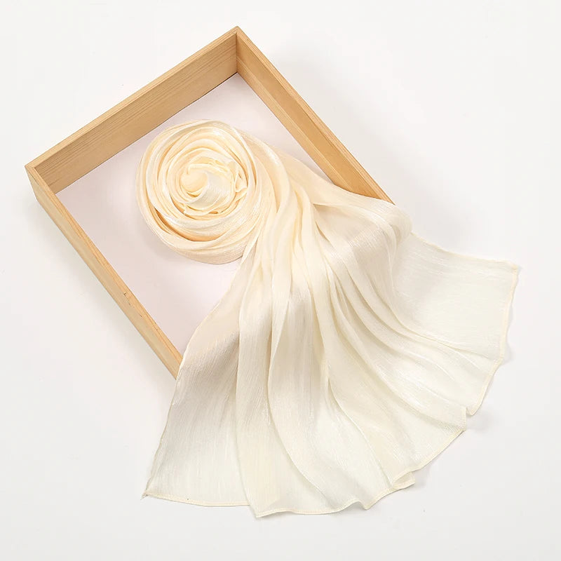 Un chal de hijab de gasa color crema con textura arrugada, exhibido en un marco de madera.