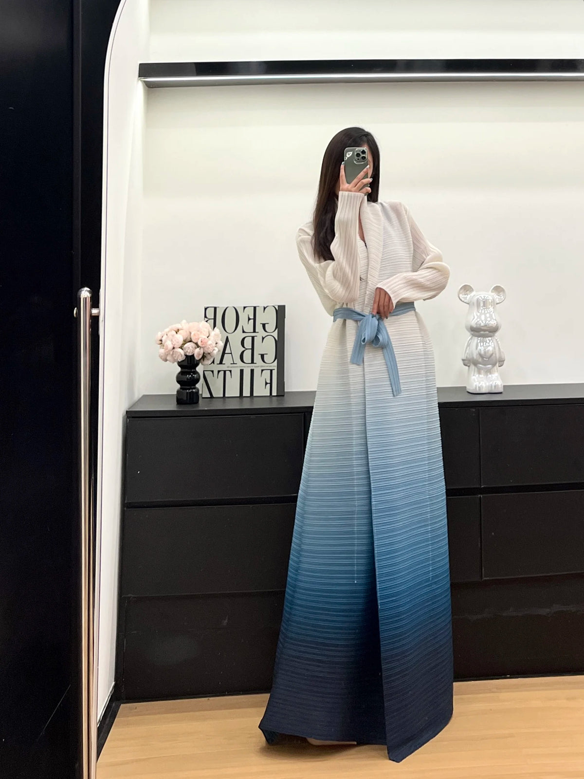 Une femme modélise un trench-coat à plis bleu clair et blanc dans un studio.